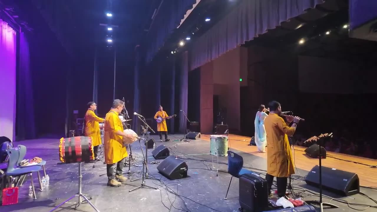 Live band performing on a theater stage with wedge monitors and microphones