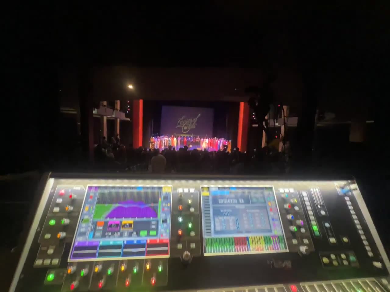 Digital console at front of house facing a lit theater stage during a Christmas cantata