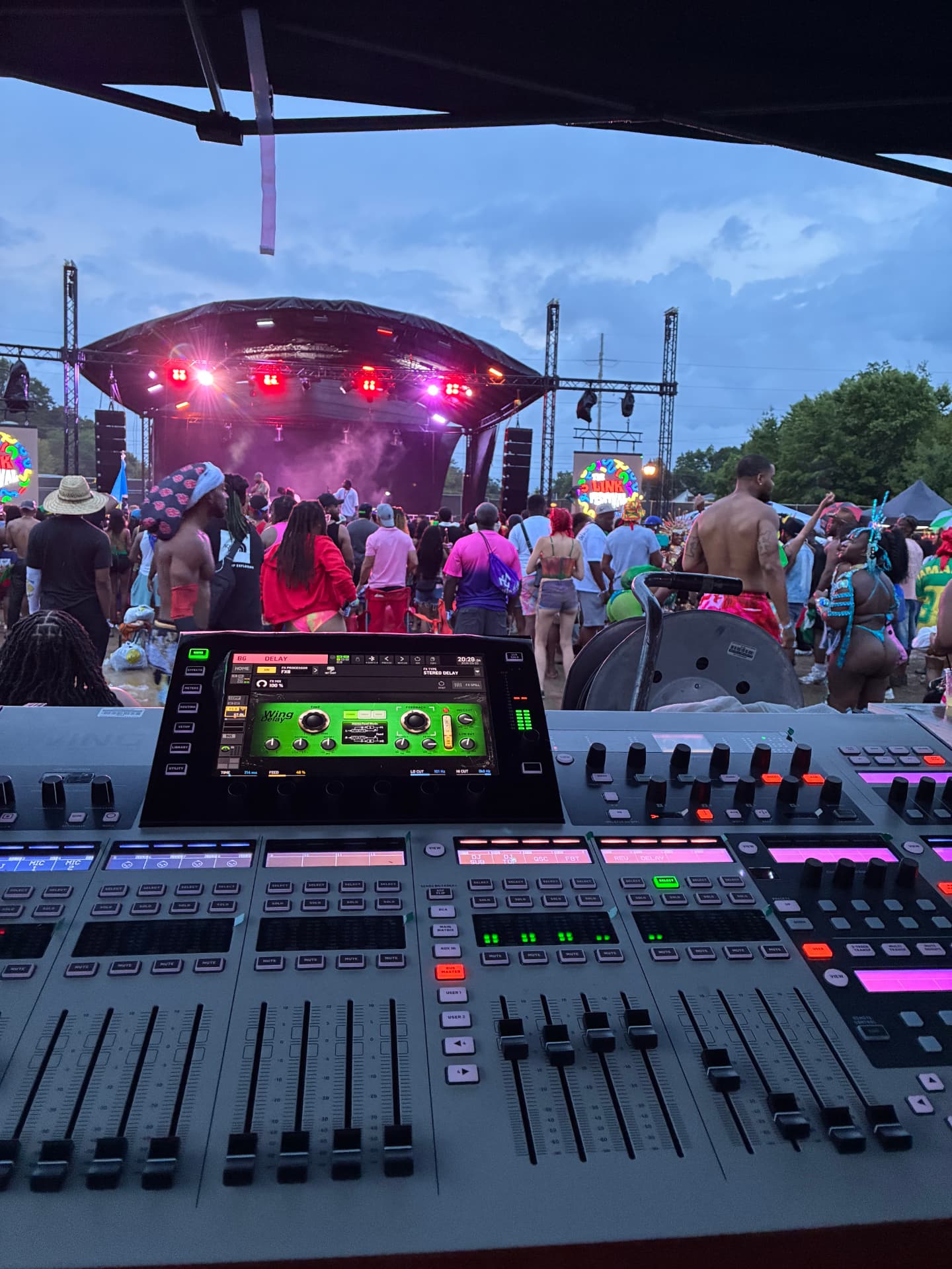 Outdoor festival main stage at dusk seen from the FOH mixing position with a digital console in the foreground