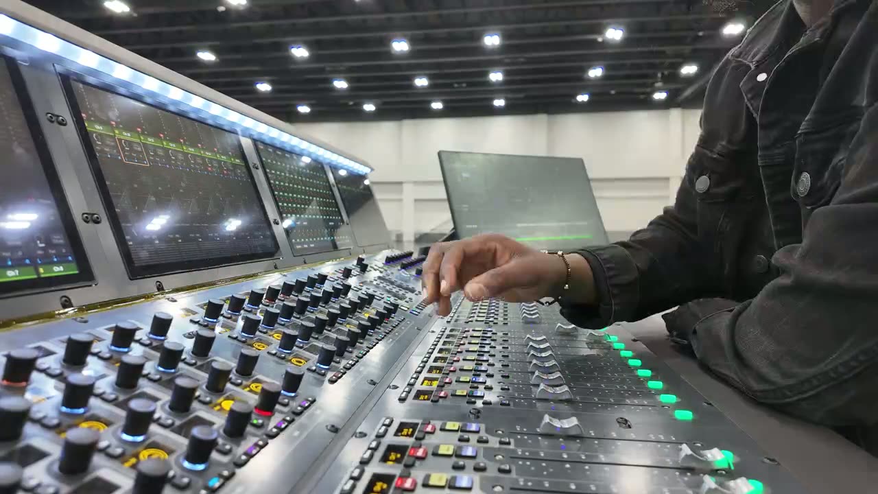 Engineer's hand on the faders of a large mixing console at front of house
