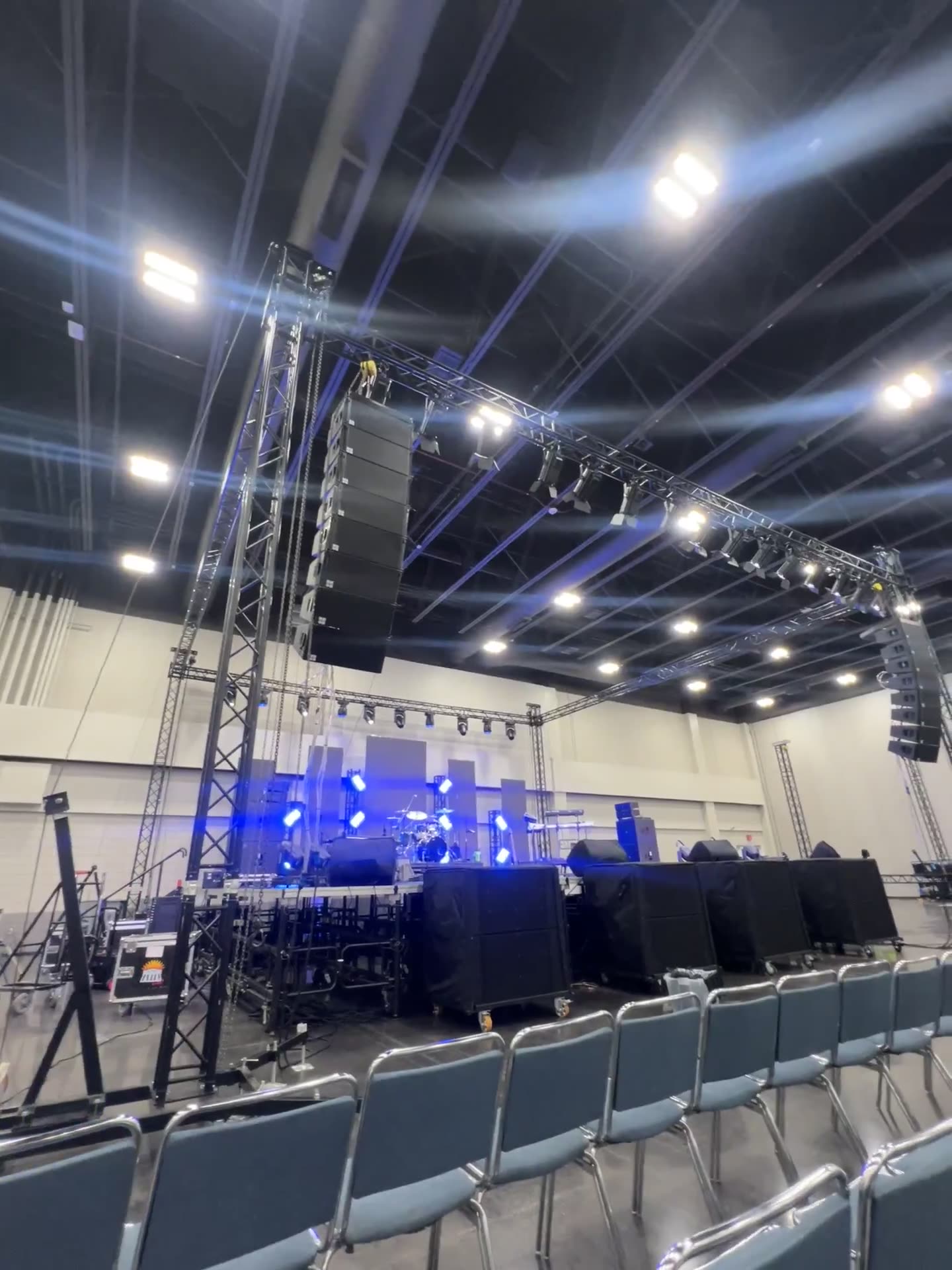 Flown line array and lighting truss over a blue-lit stage with seating